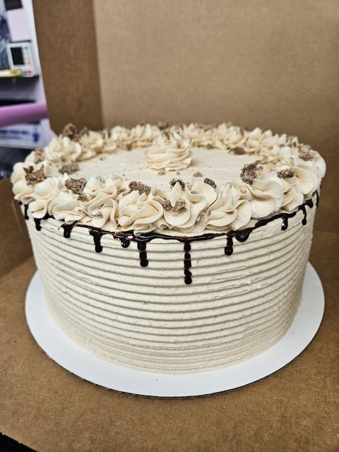 Round layer cake with ridged peanut butter frosting, piped rosettes and a chocolate drip, in an open bakery box