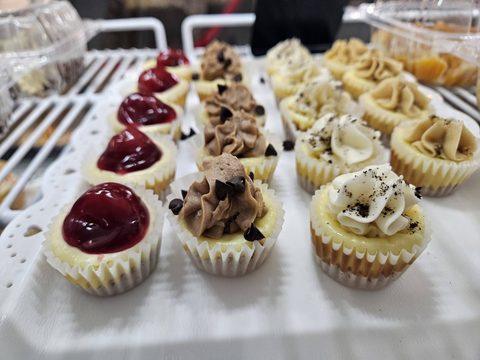 Mini cheesecakes with cherry topping and piped chocolate and vanilla frosting on a tray in the bakery case
